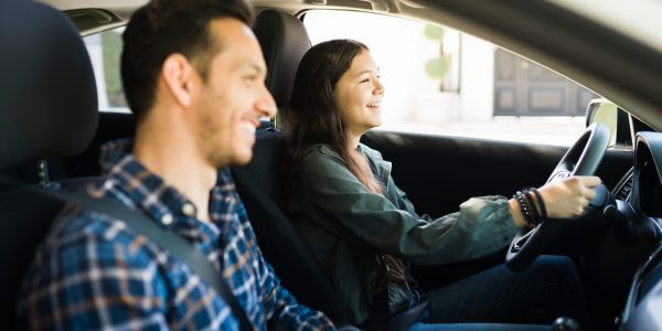Happy handsome dad and teen daughter laughing while driving. Adolescent girl practicing her driving skills with her father